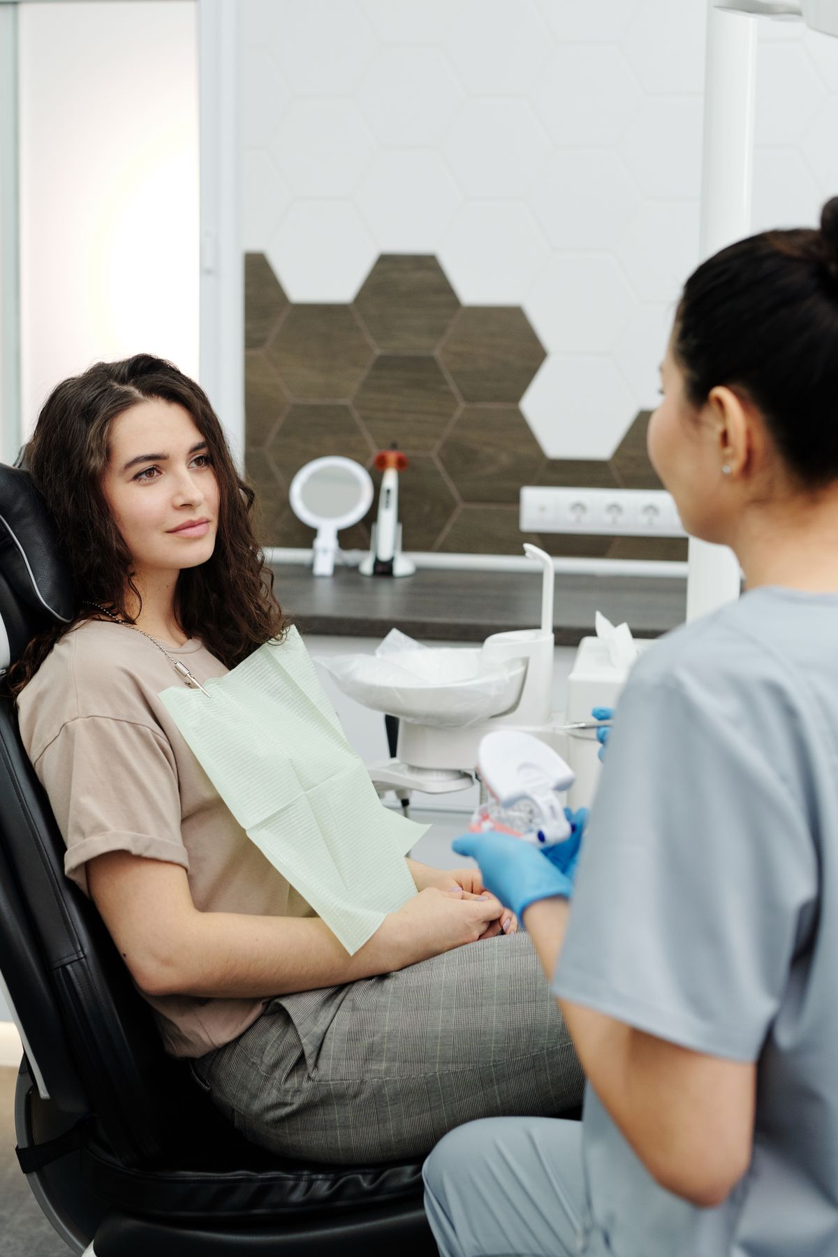 A smiling patient in a dental chair talking with a clinician holding a teeth model