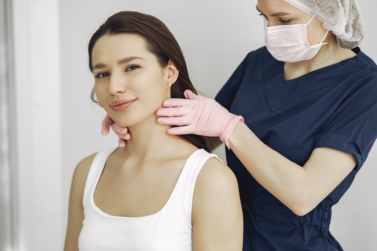 A gloved practitioner examining the neck skin of a smiling patient in a bright exam room