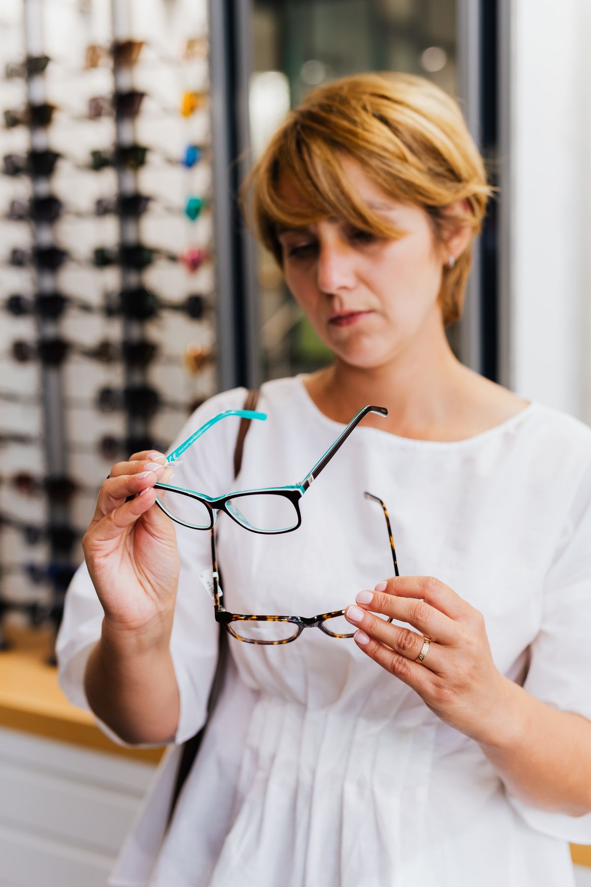 A woman comparing eyeglass frames in a bright optical shop