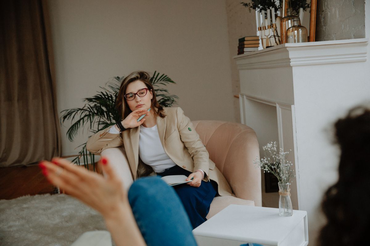 A therapist with a notebook listening from an armchair in a bright consulting room