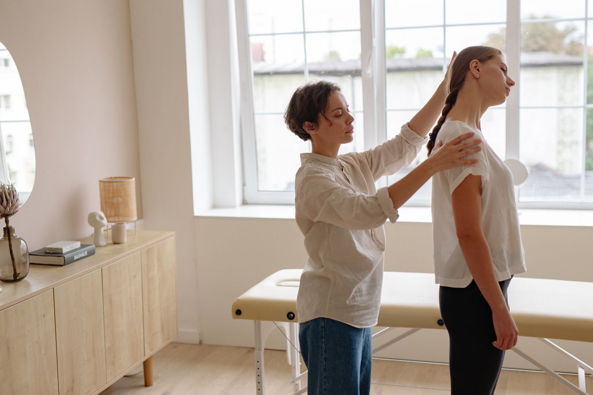 A practitioner assessing a standing patient’s posture in a warm treatment room
