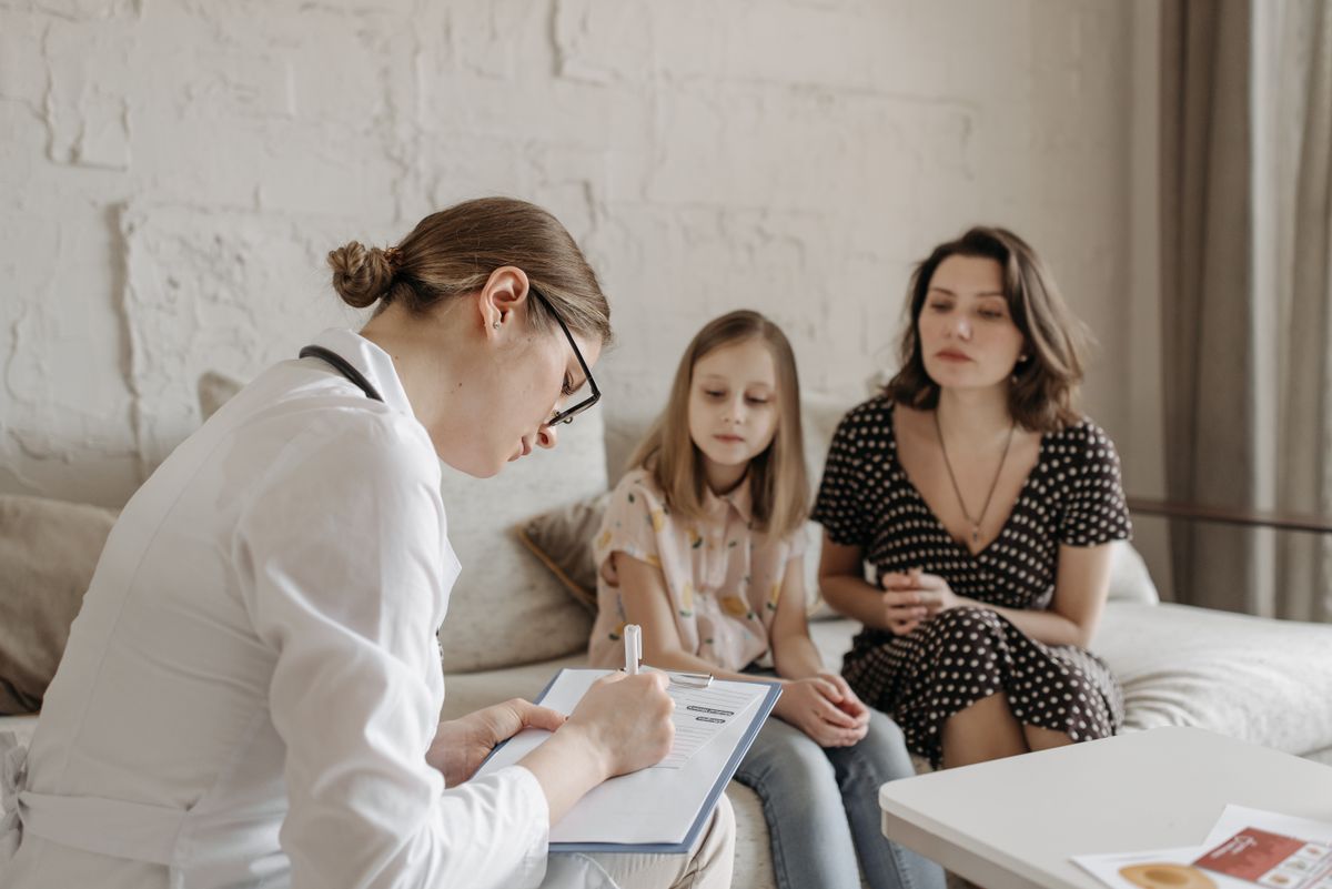 A family physician taking notes with a mother and daughter during a consultation