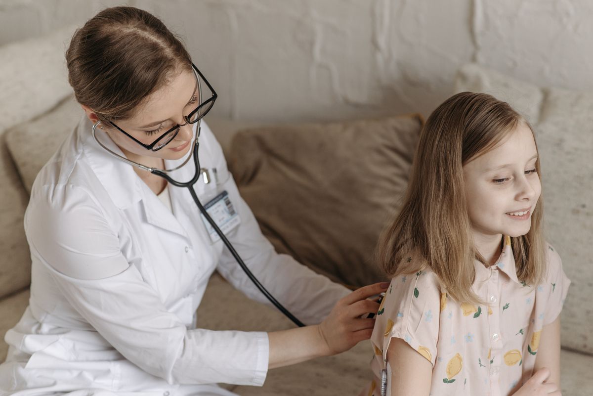 A doctor listening to a smiling young girl's breathing with a stethoscope