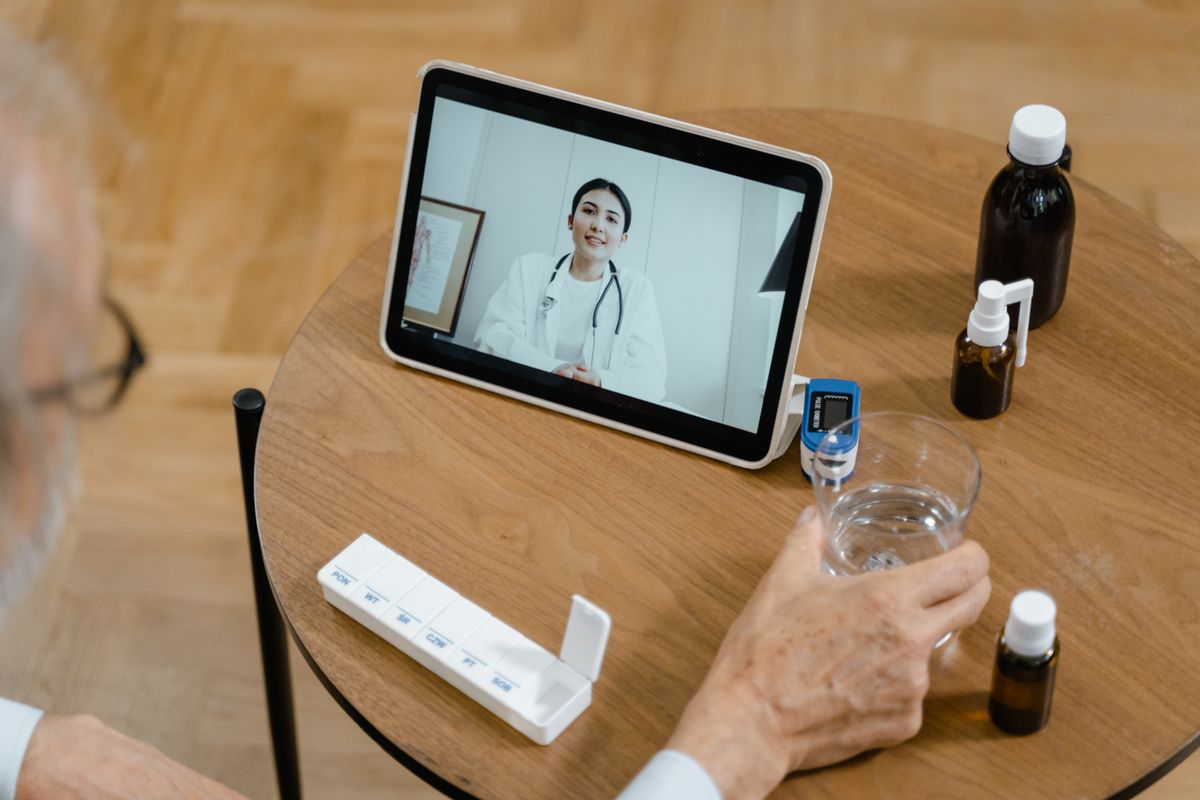 A patient at home on a video call with a doctor on a tablet, beside medications